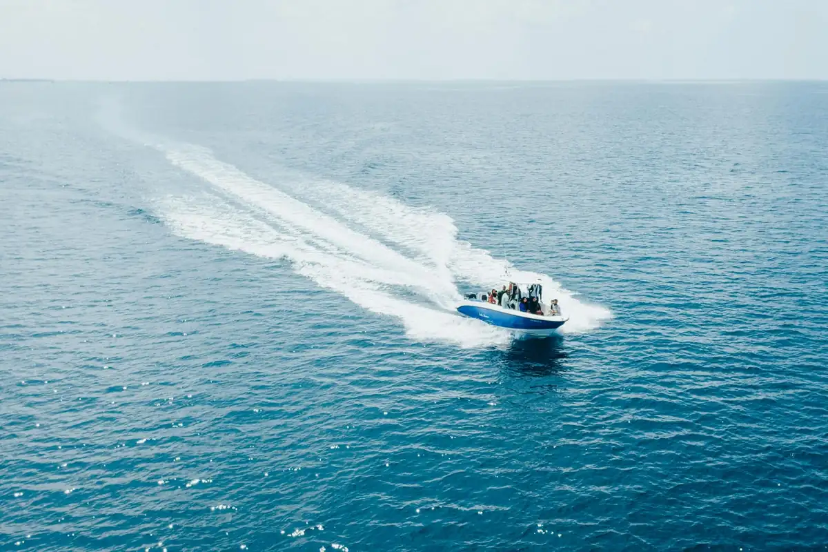 A speedboat seen from above, leaving a long white wake across the open sea