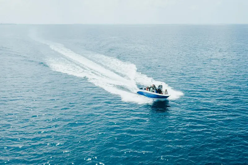 A speedboat seen from above, leaving a long white wake across the open sea