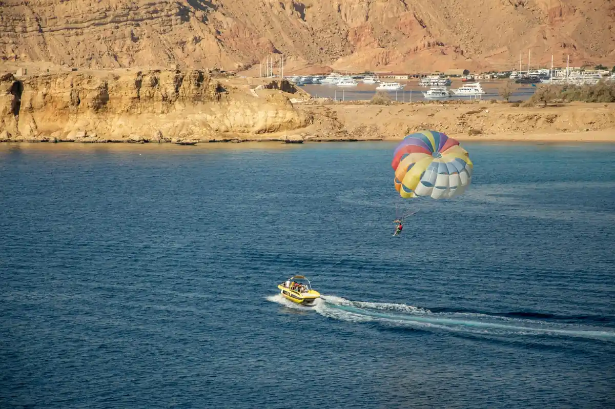 A striped parasail towed across the bay, the marina and sandstone cliffs behind
