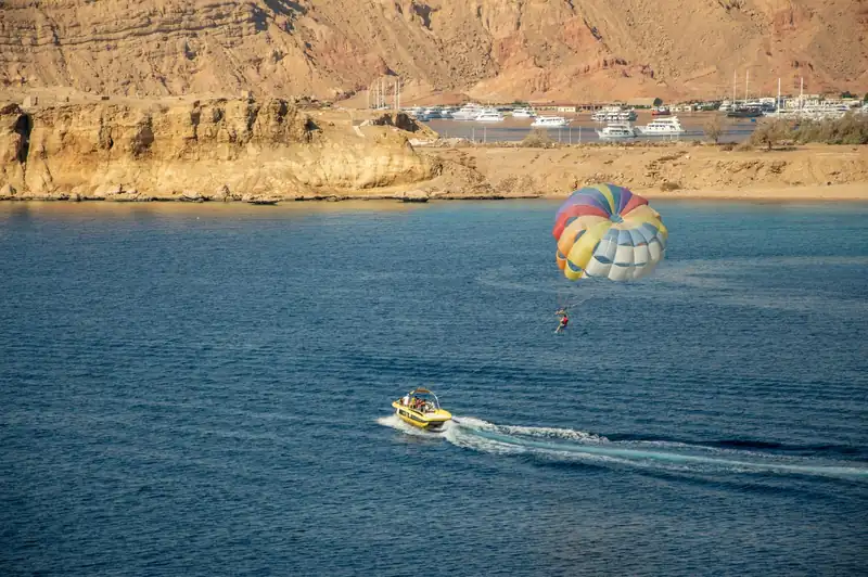 A striped parasail towed across the bay, the marina and sandstone cliffs behind