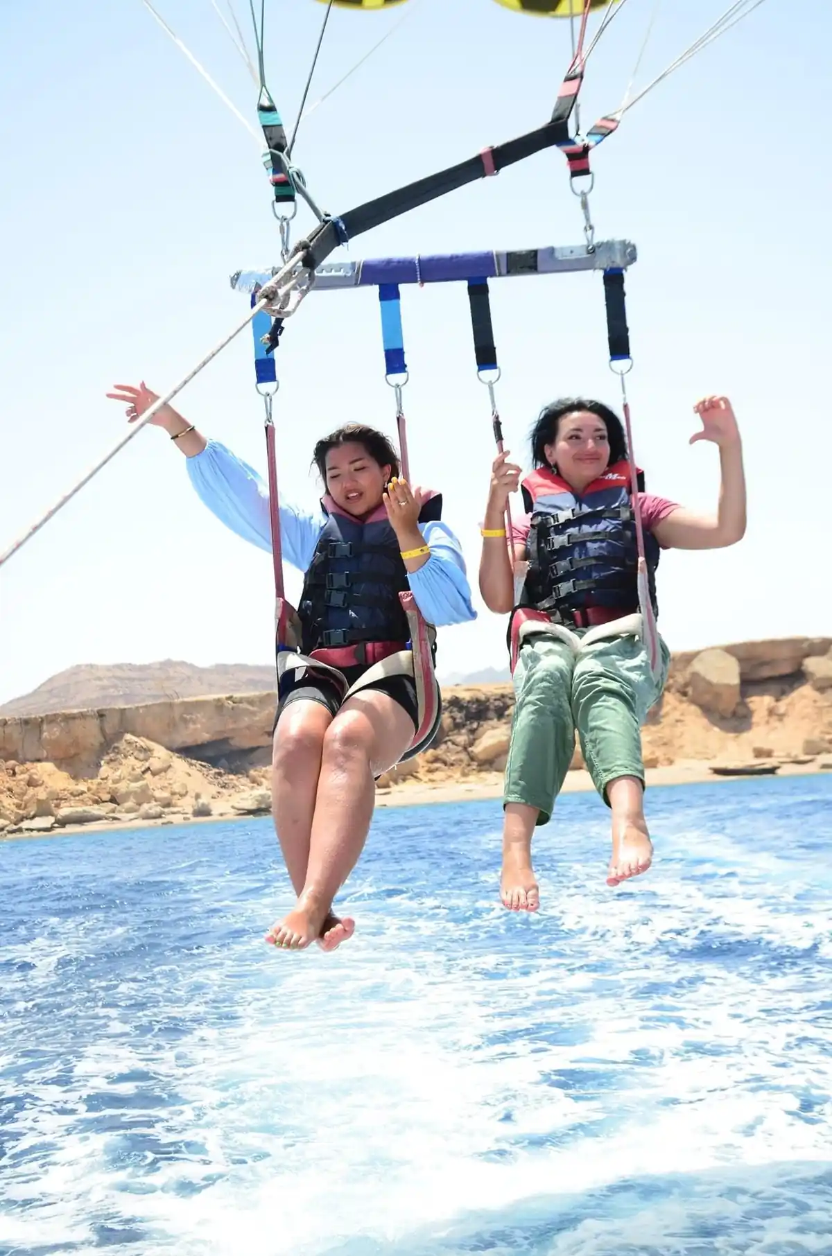 Two riders lifting off over the boat's wake, desert cliffs behind