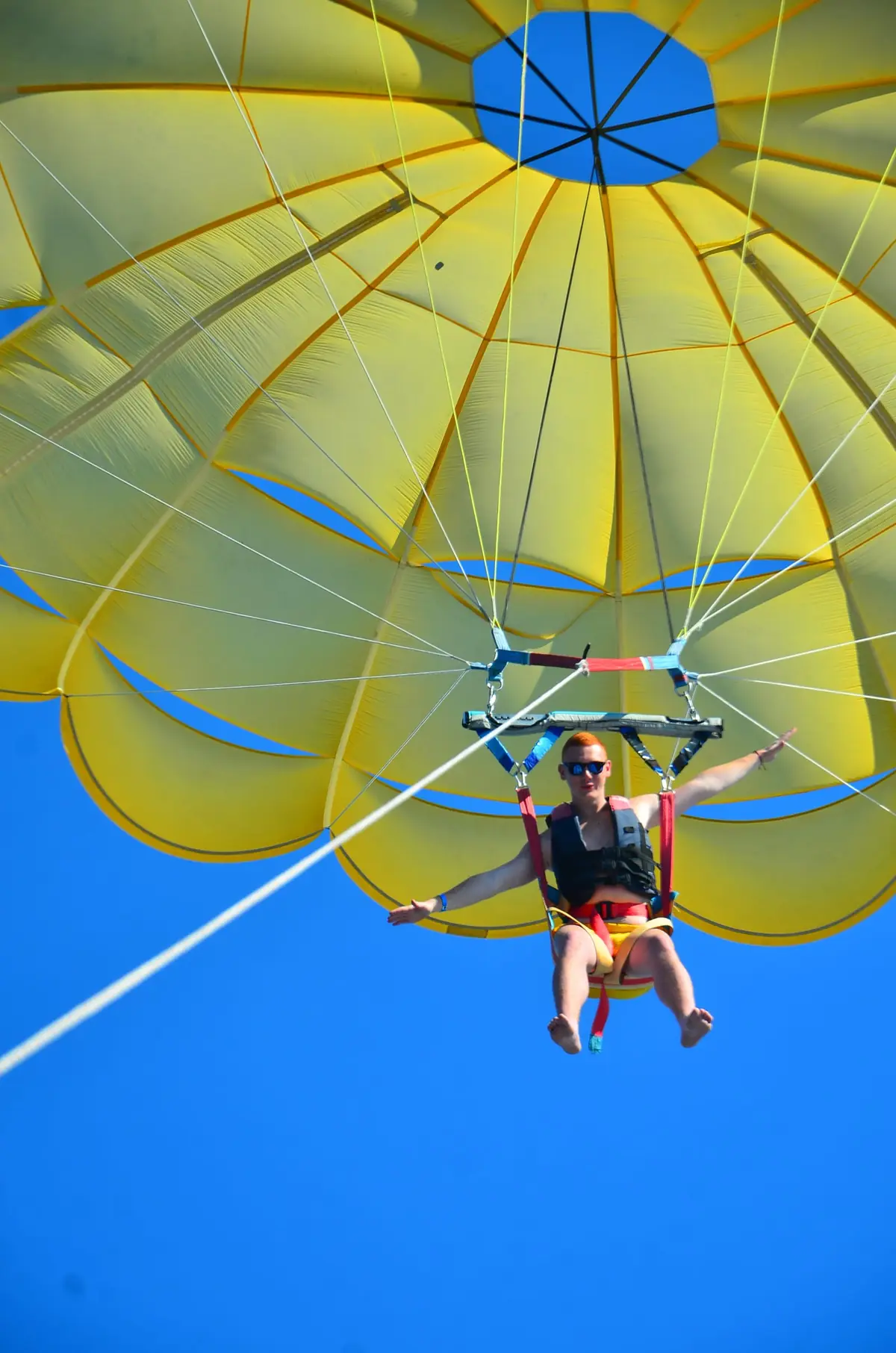 A parasailing rider in the harness under a yellow canopy