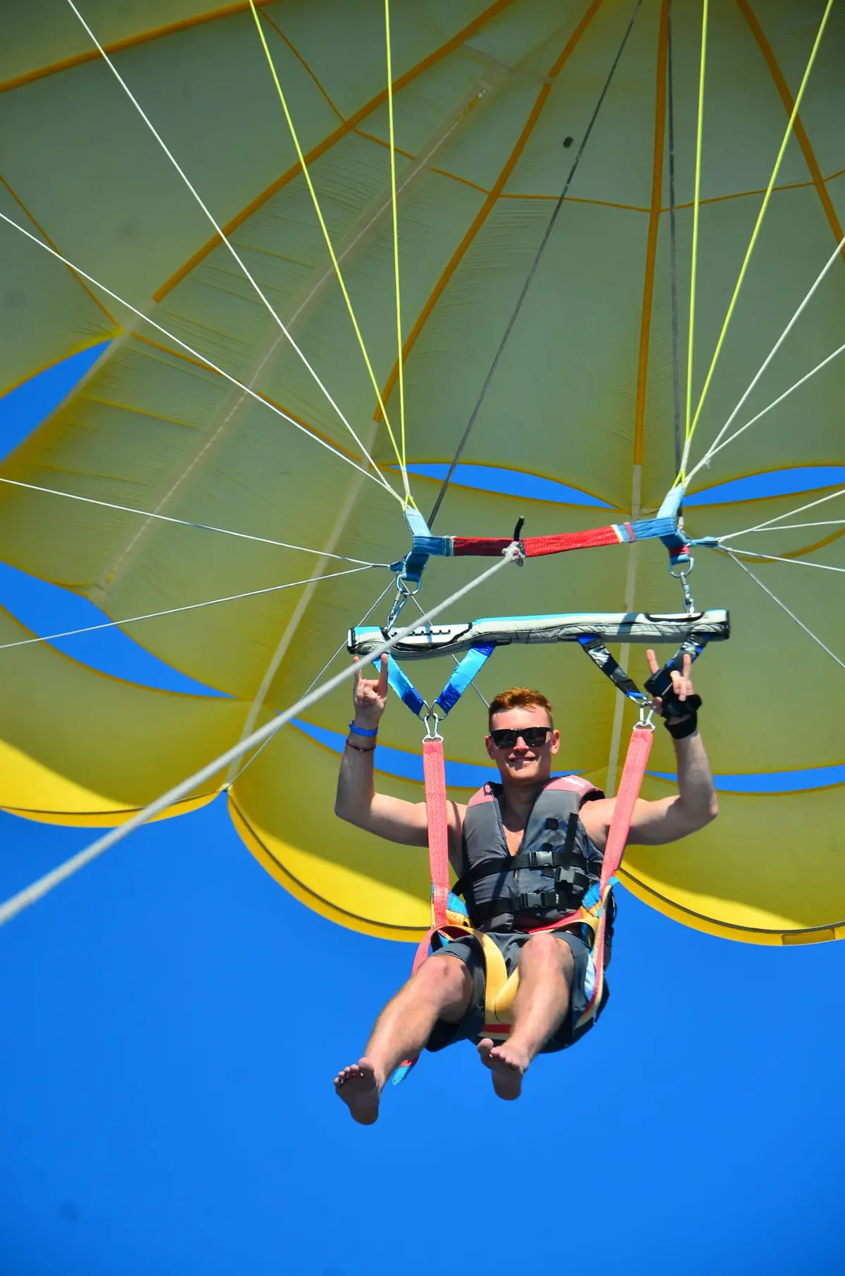 A parasailing rider with both arms up under a yellow canopy