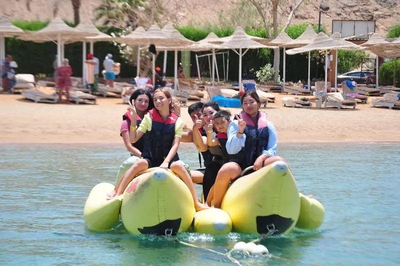 A group in life jackets on a yellow banana boat by the beach