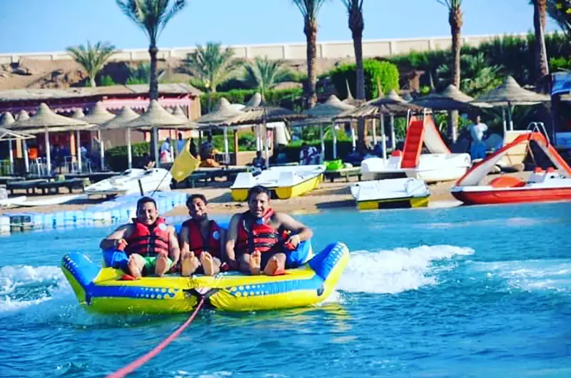 Three riders on a towed inflatable, a hotel beach and palms behind