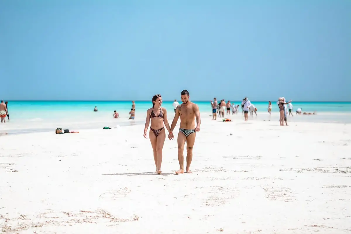 A couple walking hand in hand on the White Island sandbar, other swimmers in the turquoise shallows behind