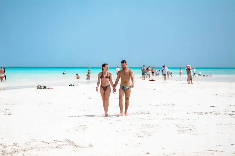 A couple walking hand in hand on the White Island sandbar, other swimmers in the turquoise shallows behind