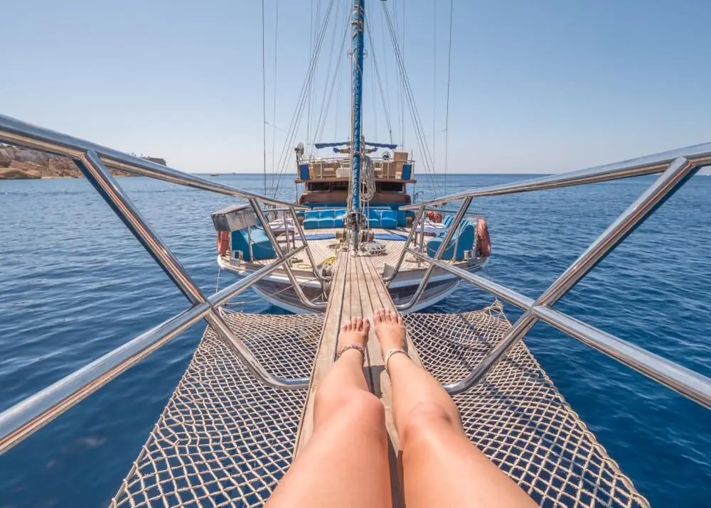 A guest's legs stretched out on the bow net, looking back along the deck to the mast