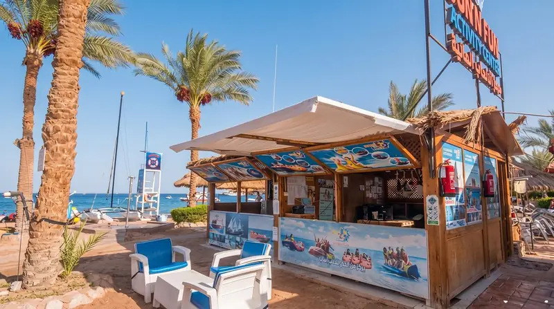 A water sports kiosk with a striped awning under palm trees on the beach