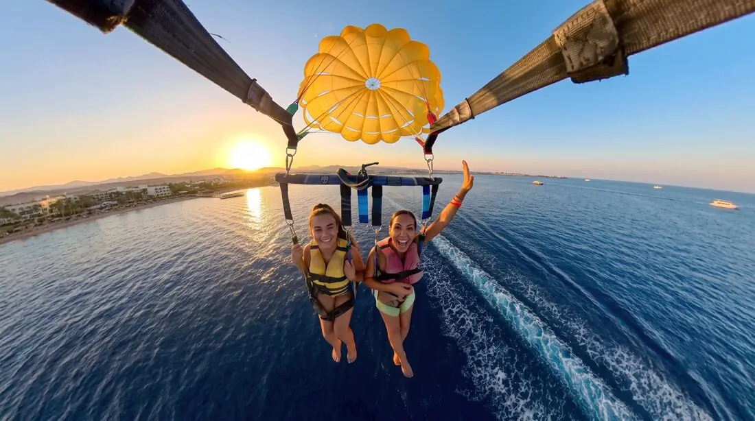 Two parasailers waving under a yellow canopy at sunset, high over the bay