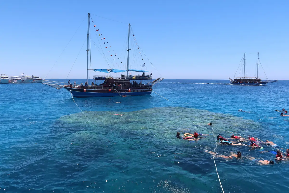 A two-masted pirate galleon flying flags over the reef, with snorkellers holding a line beside it