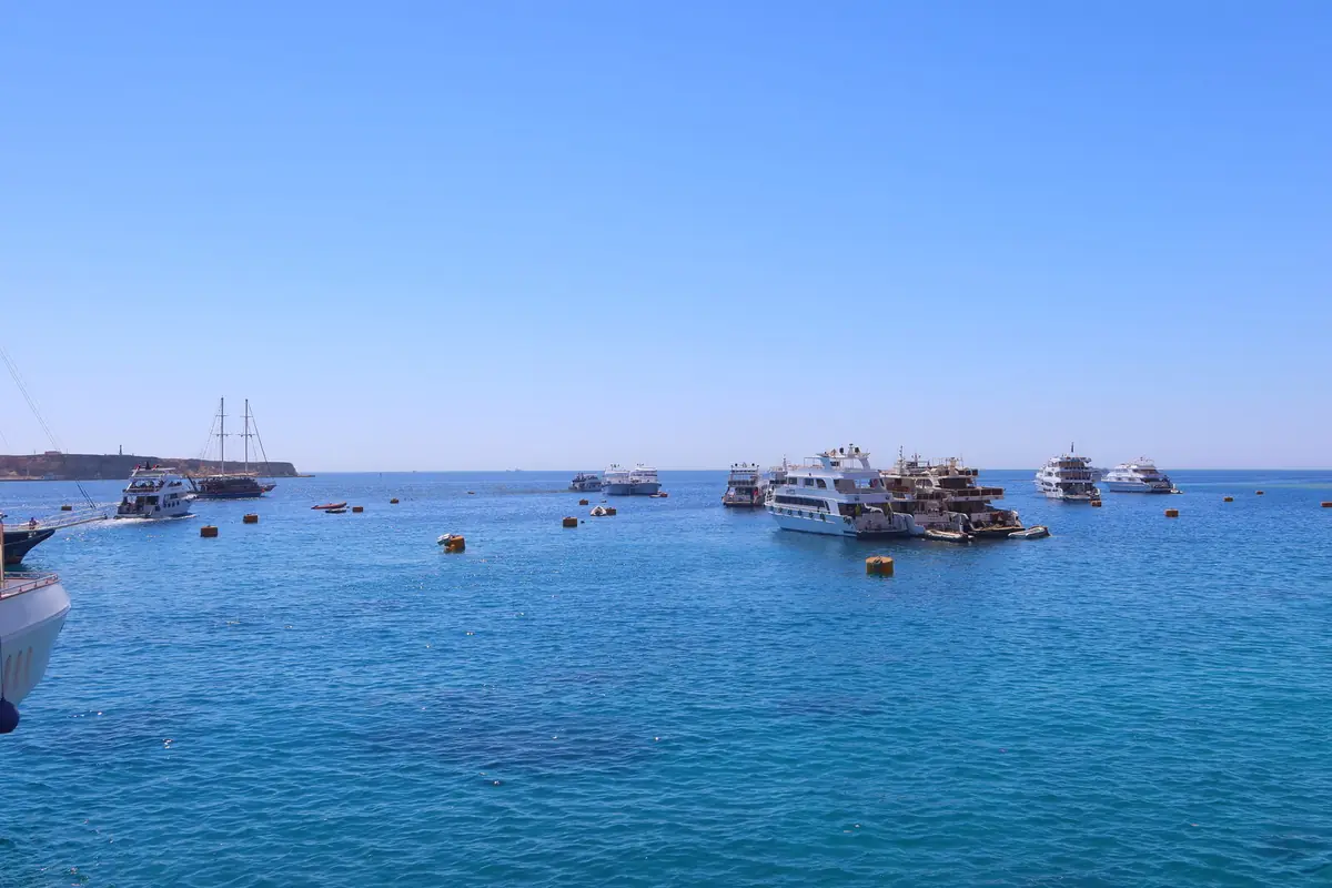 Boats at anchor on open blue sea, with a galleon on the horizon
