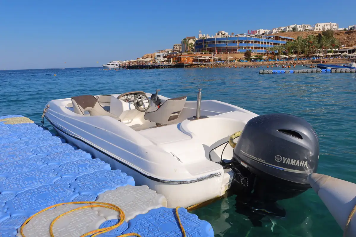 A white speedboat with an outboard engine at a floating pontoon, hotels along the shore