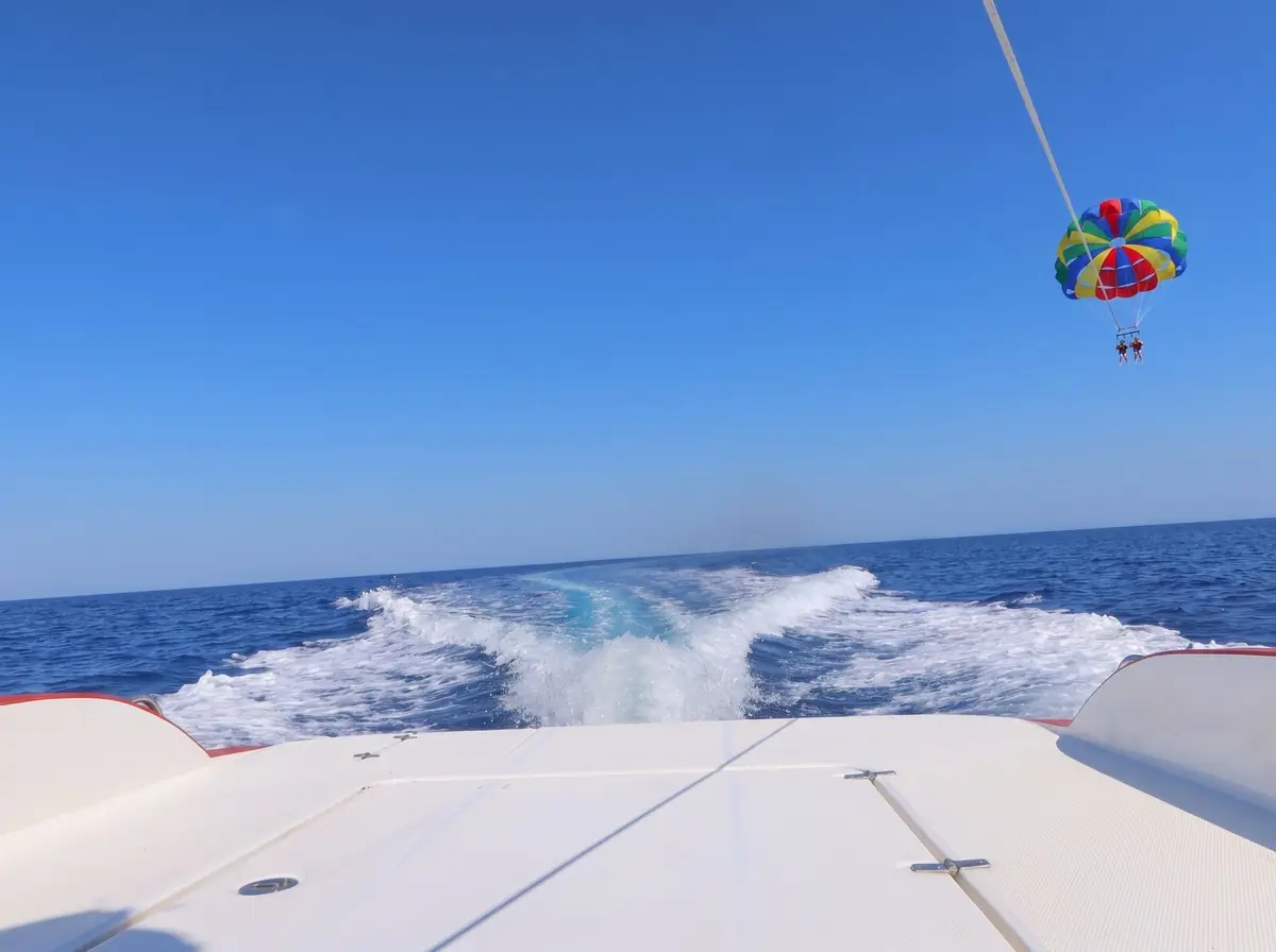 A rainbow parasail high in the sky, seen from the stern of the speedboat above its wake