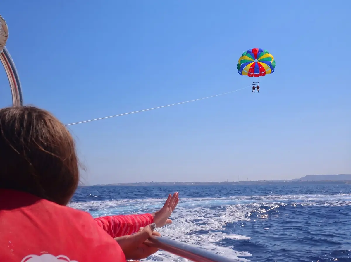 A young guest on the boat deck, seen from behind, waving at the parasail