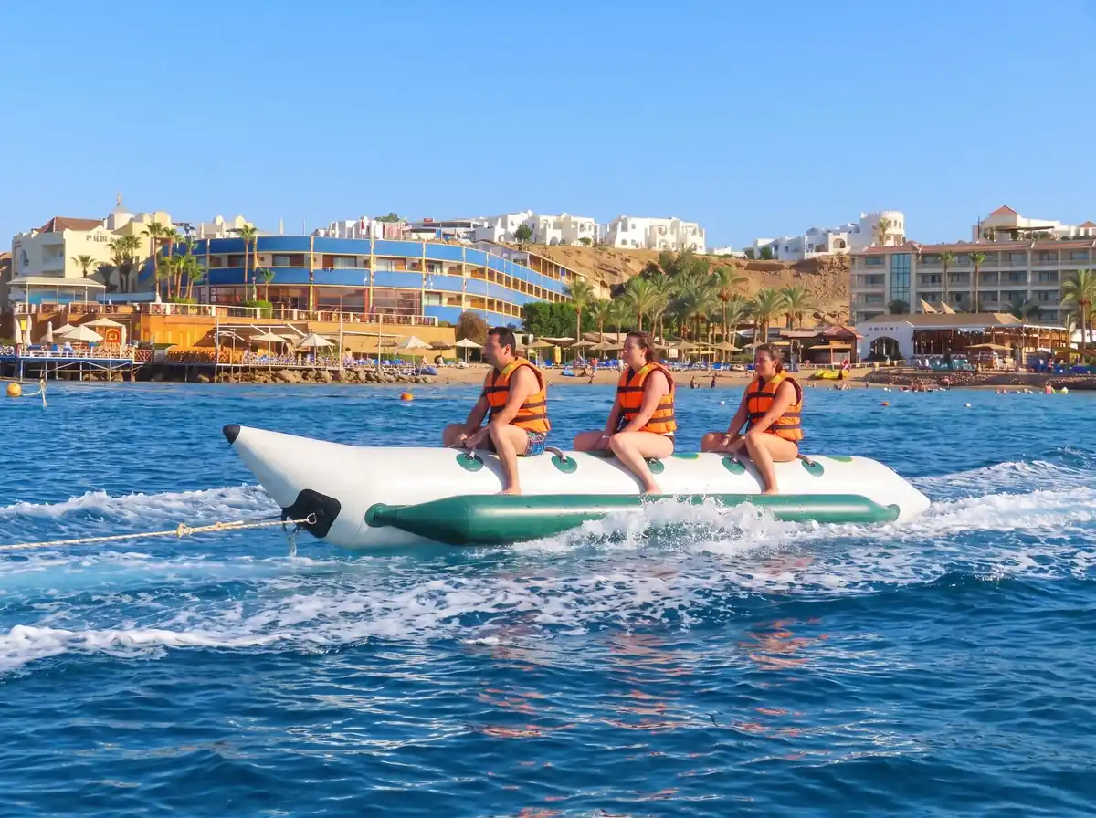Three riders on a banana boat on the bay, with hotels behind