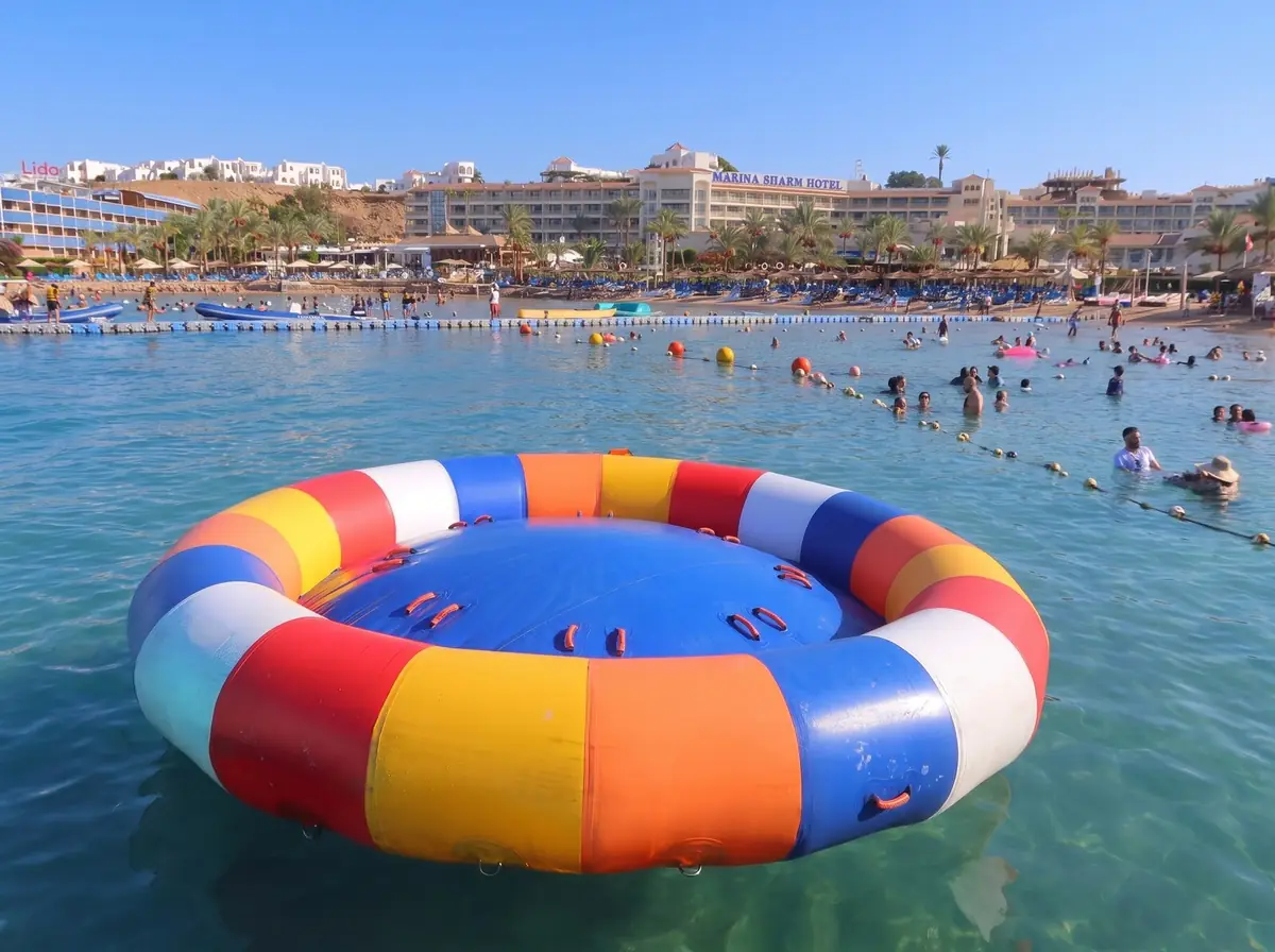 An empty striped ringo tube on the water, with the beach and swimmers behind