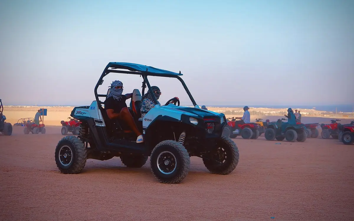 Un buggy Polaris nel deserto, con le persone a bordo in foulard e occhiali, e i quad dietro