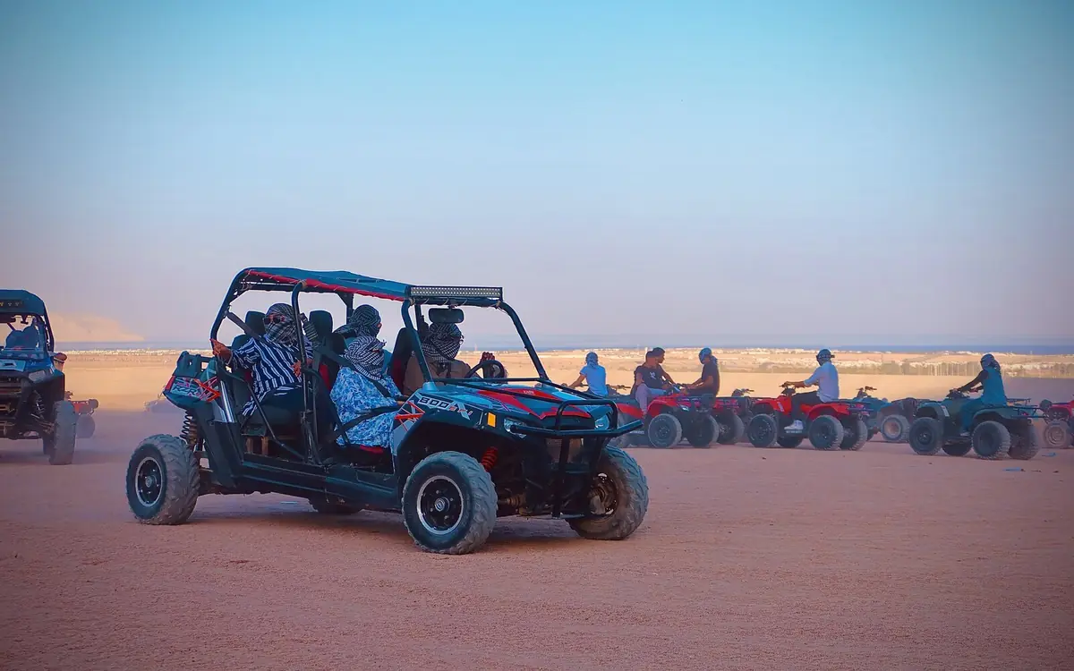 Un buggy a quattro posti con persone che indossano il foulard beduino, e una fila di quad dietro