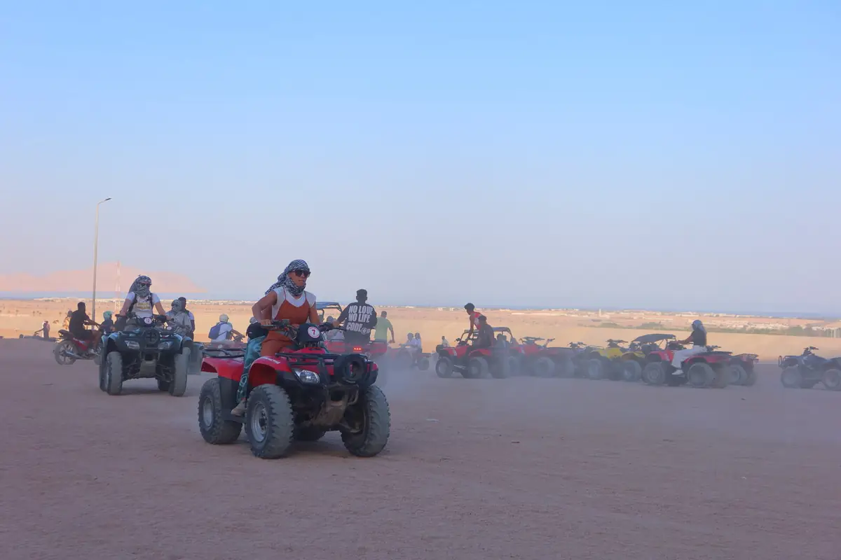 Persone in quad con foulard e occhiali da sole che attraversano la sabbia