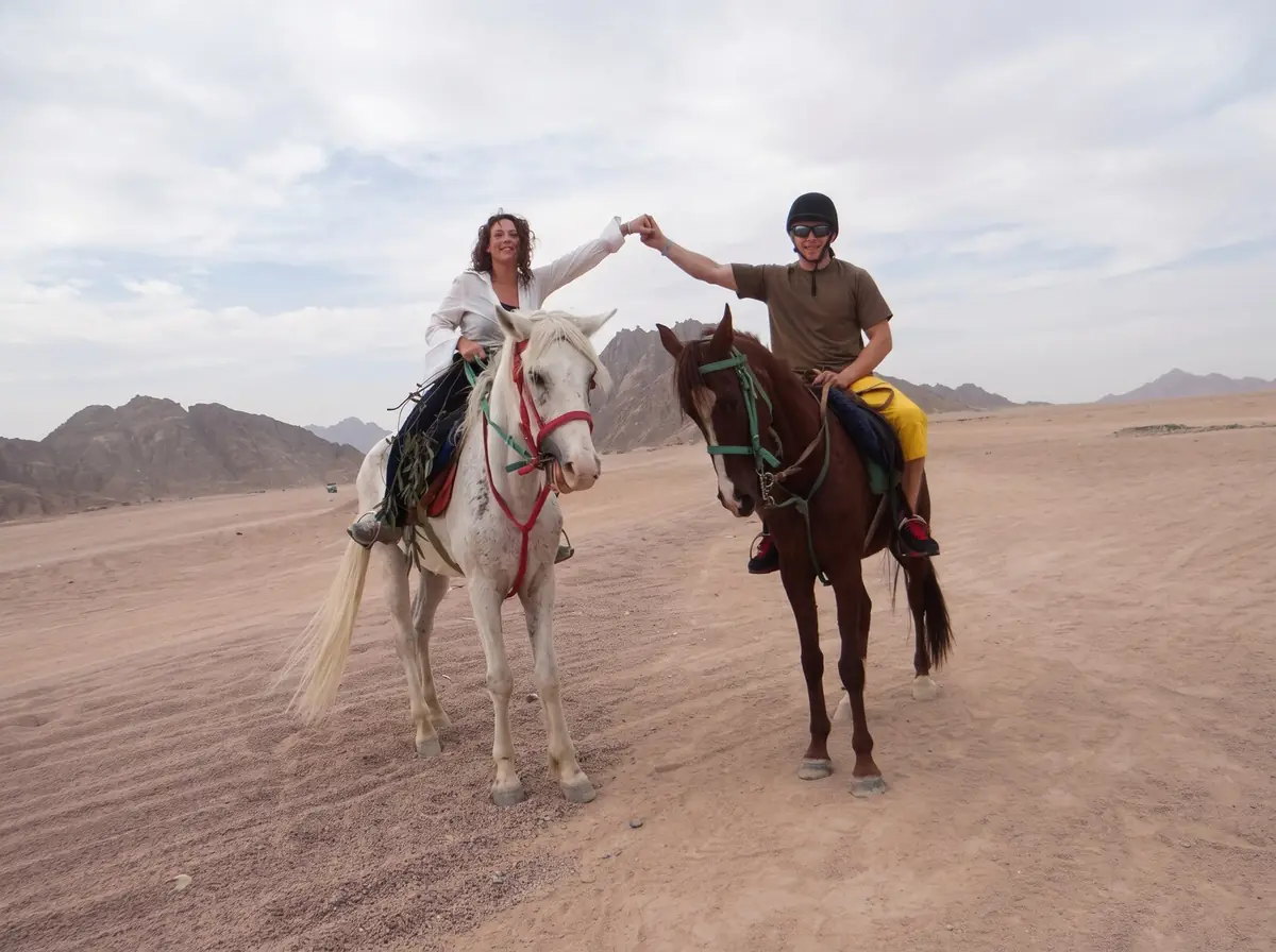 Due persone a cavallo che si tengono per mano tra i loro cavalli, nel deserto