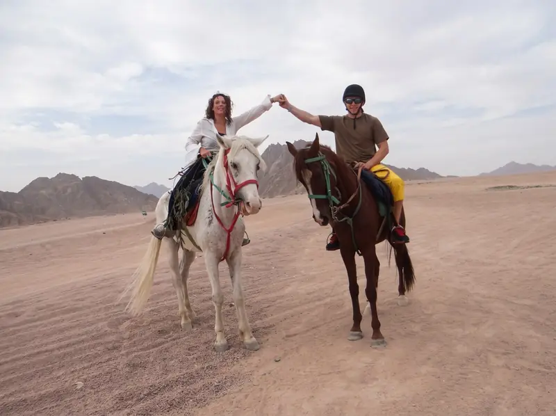 Two riders holding hands between their horses in the desert