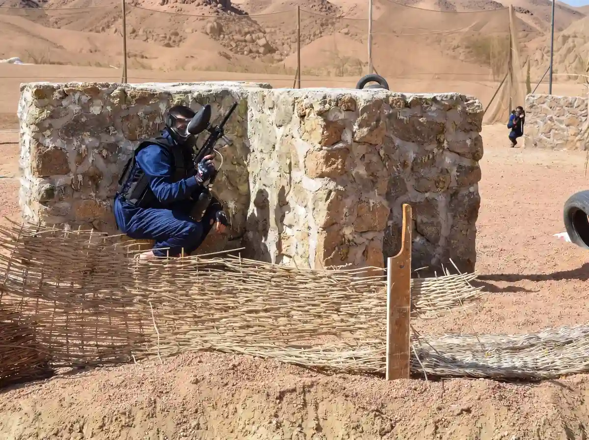 A masked paintball player crouching behind a stone bunker