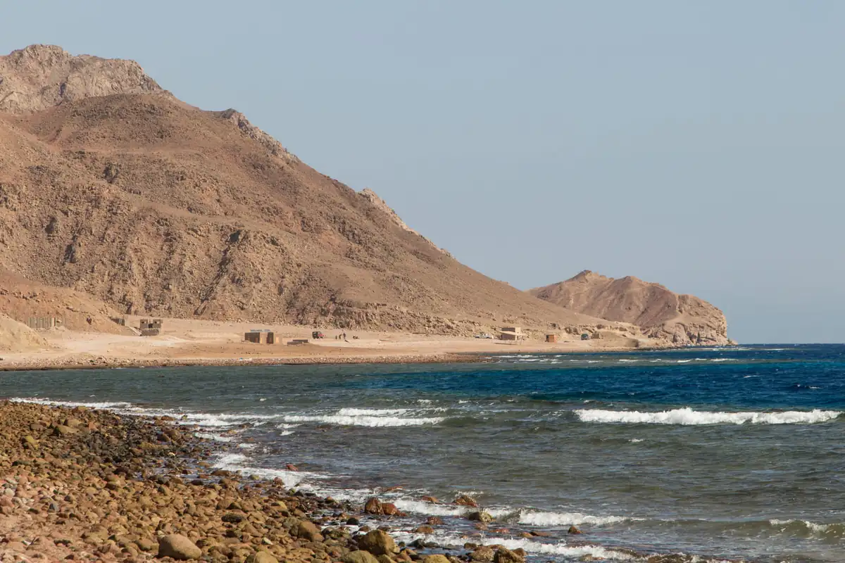 Waves on a pebble shore under bare desert mountains on the Sinai coast
